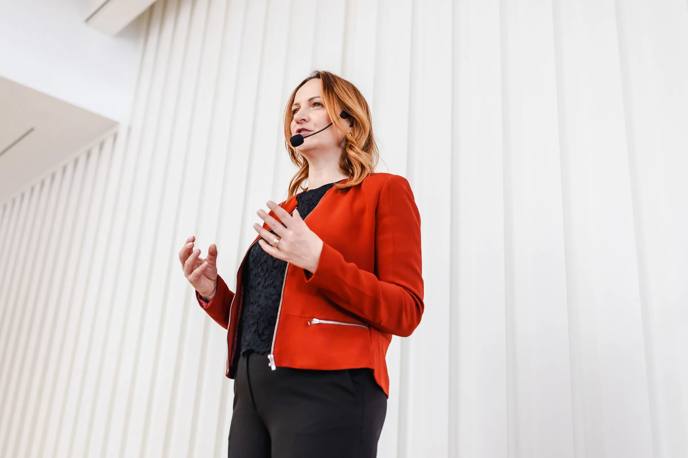 Maria Mync is speaking on stage as a keynote speaker, wearing a headset microphone